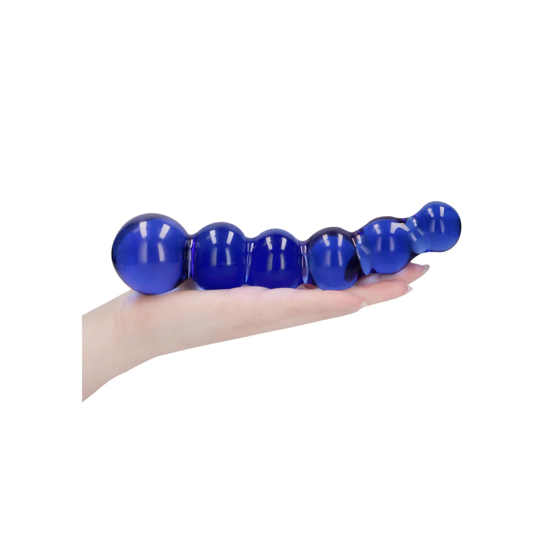 Hånd holder en blå, strukturert glassdildo med kuler, egnet for temperaturlek.
