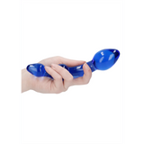 Hånd holder en blå glassdildo med to buler, den ene større enn den andre.