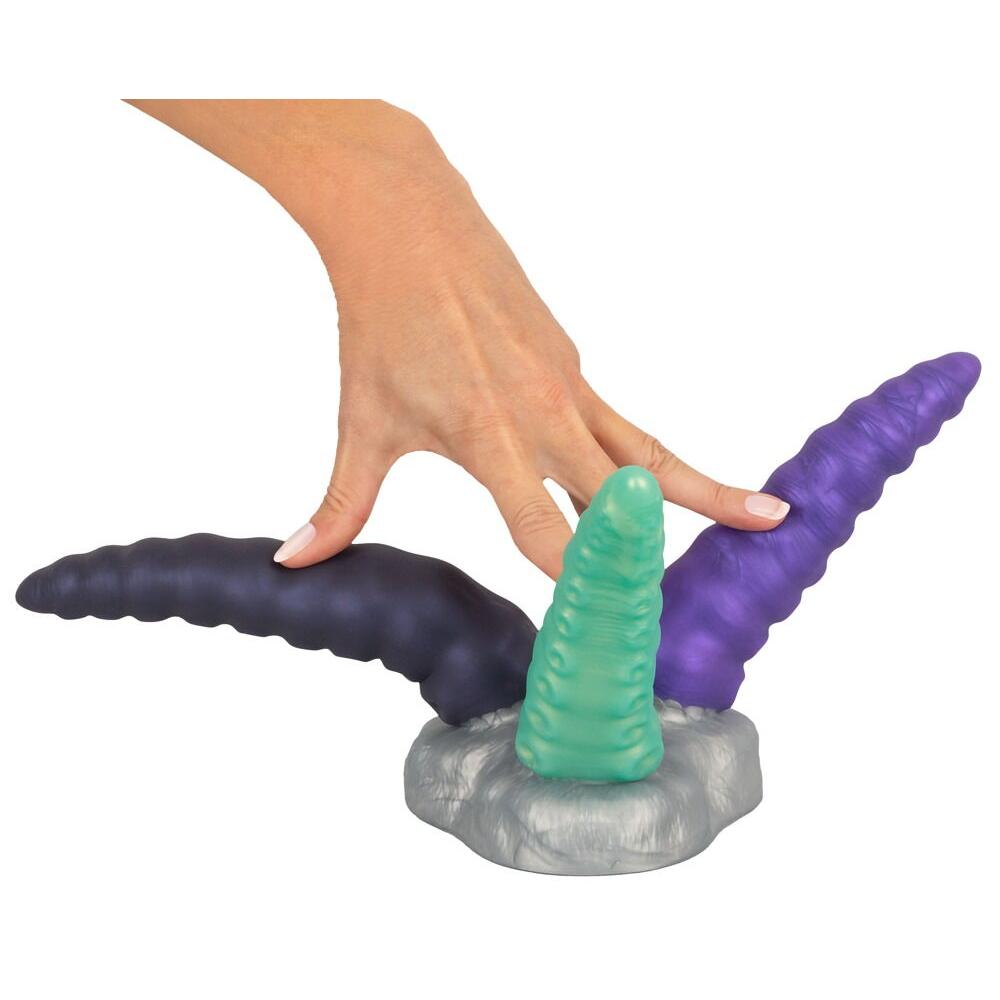 En hånd holder en Triple Tentacle fantasidildo med tre fleksible armer i lilla, grønt og mørkegrått silikon.