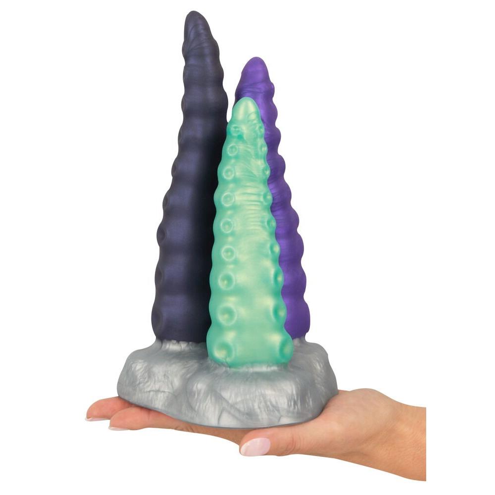 Hånd holder Triple Tentacle fantasidildo med tre fleksible armer i lilla, grønt og mørk lilla silikon.