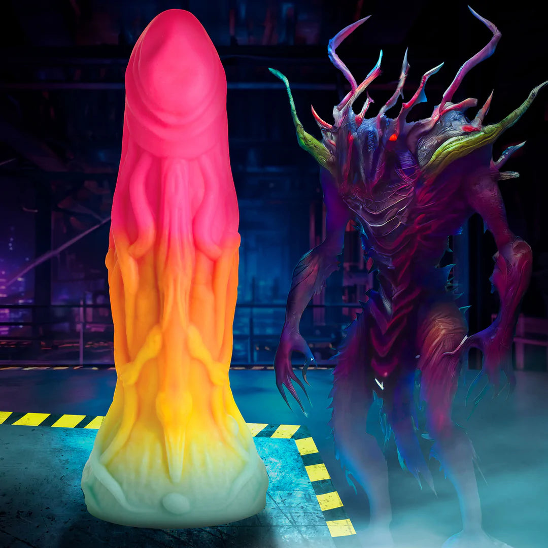 Regnbuefarget Shape Shifter alien-dildo med årete kropp og et mystisk øgleansikt, ved siden av en mørk alien-figur.