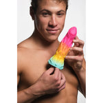 Mann holder en regnbuefarget Shape Shifter Alien Fantasy Dildo med årete kropp og øgleansikt.