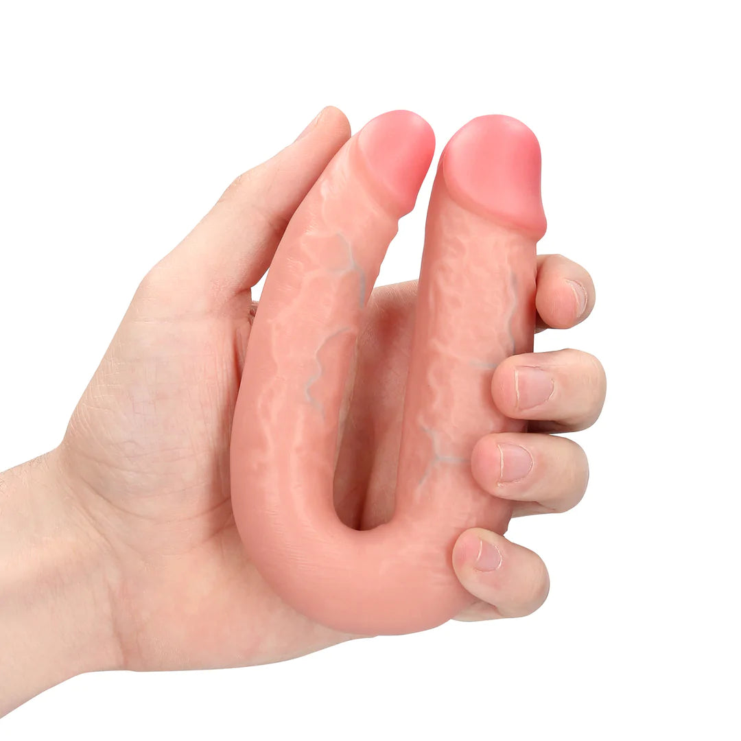 Kjøttfarget U-formet dobbeldildo i realistisk design med årer, holdt i en hånd.