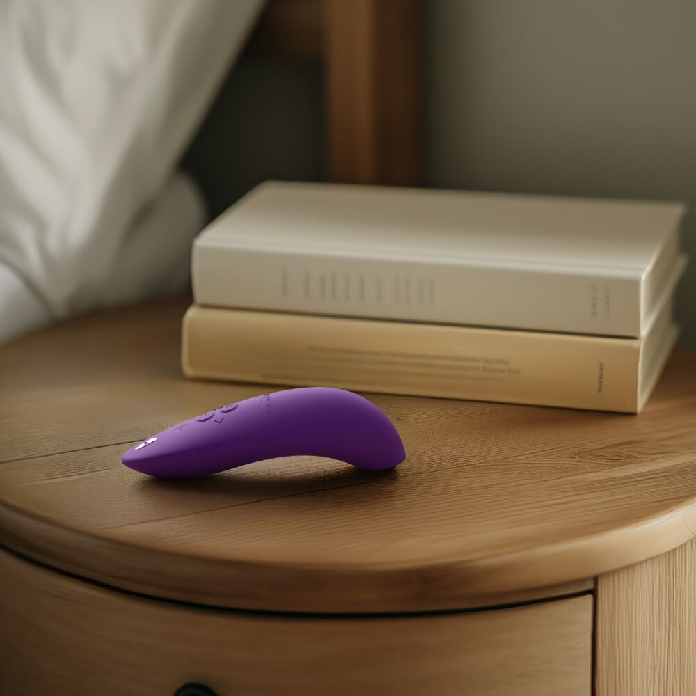 Lilla We-Vibe Melt 2 lufttrykksvibrator i silikon på et nattbord med bøker i bakgrunnen.