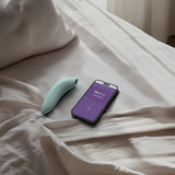 We-Vibe Melt 2 lufttrykksvibrator i dus grønn silikon, ved siden av en smarttelefon med appen.