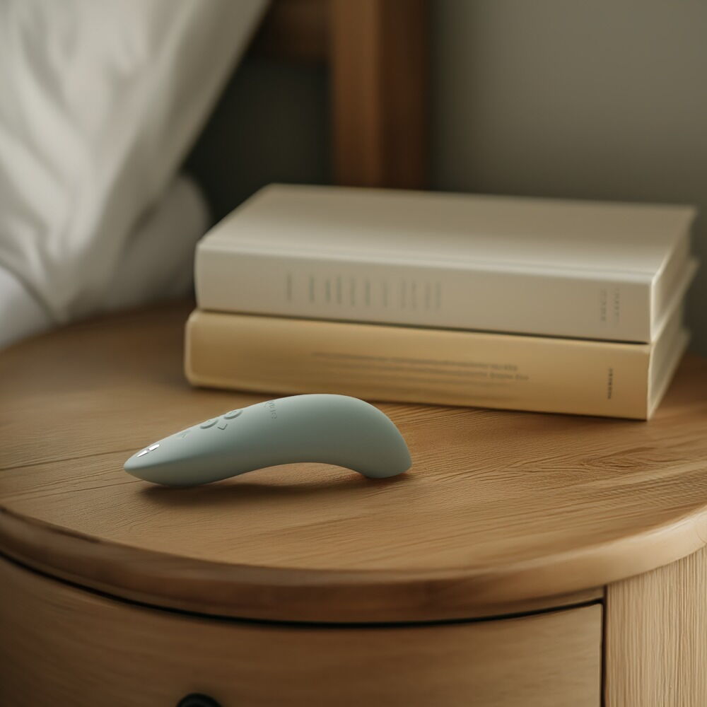 We-Vibe Melt 2 lufttrykksvibrator i dus grønn silikon, ergonomisk formet, på et nattbord.