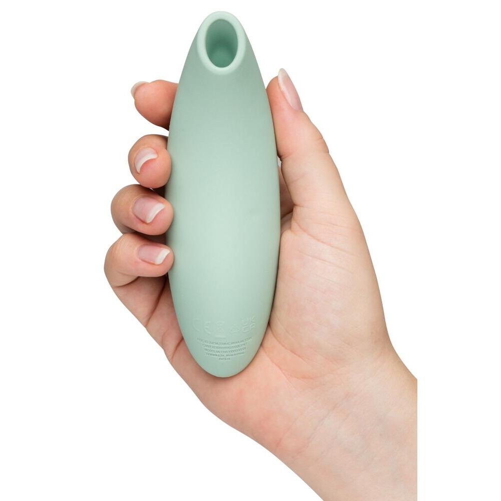 We-Vibe Melt 2 lufttrykksvibrator i dus grønn silikon, holdt i en hånd, med oval form og åpen tupp.