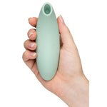 We-Vibe Melt 2 lufttrykksvibrator i dus grønn silikon, holdt i en hånd, med oval form og åpen tupp.